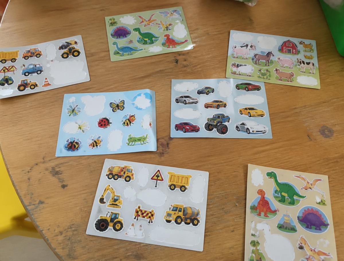 Inexpensive sticker sheets with diggers, dinosaurs, farm animals, insects and cars spread across a timber classroom table
